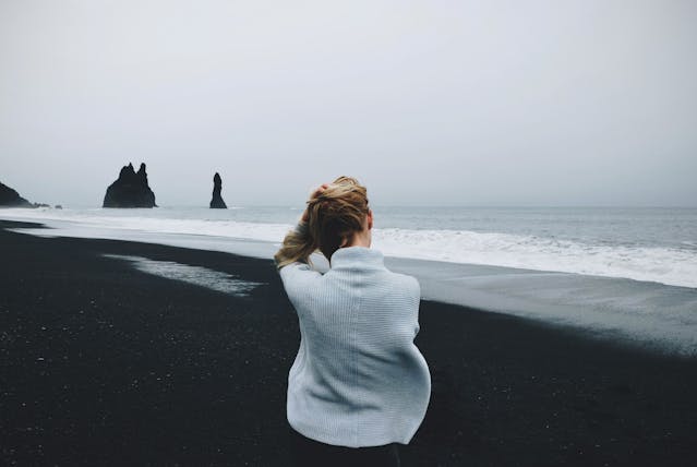 a woman from the back as she stands by the sea