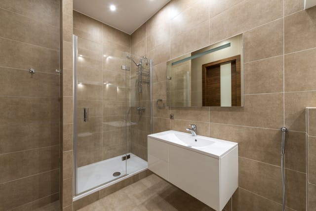 a shower and a sink in a brown tiled bathroom
