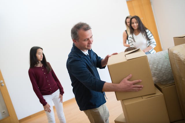 a man stacking moving boxes while his family looks on